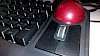 Eine Nahaufnahme des roten Trackballs und des Scrollrades auf der Tastatur, wobei man Details wie die Textur der Oberfläche und Staubpartikel erkennen kann.