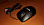 Die Amazon Basics Optische Maus zeigt ihre schlichte schwarze Oberseite mit weißem Logo, drei Tasten und dem daneben liegenden USB-Kabel auf einer orange-braunen Oberfläche. 