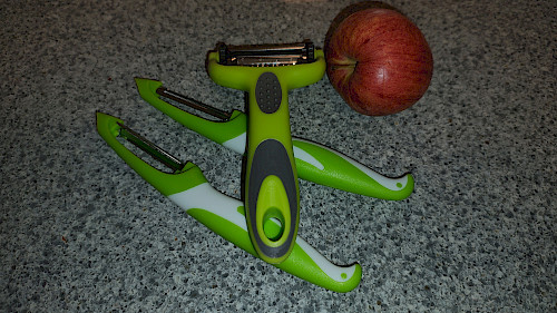 Alle drei Schäler des Mudder-Sets nebeneinander auf einer Küchenarbeitsplatte – im Vordergrund der 3-in-1-Drehschäler, daneben der Julienne- und der gerade Schäler, mit einem Apfel als Größenvergleich.
