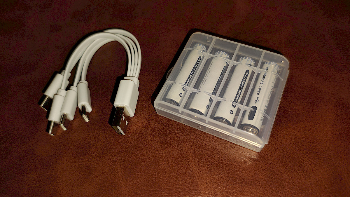 Lieferumfang im Detail: Vier AAA-Akkus in einer Kunststoffbox, daneben das 4-in-1 USB-C-Ladekabel.