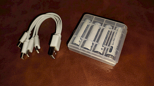 Lieferumfang im Detail: Vier AAA-Akkus in einer Kunststoffbox, daneben das 4-in-1 USB-C-Ladekabel.